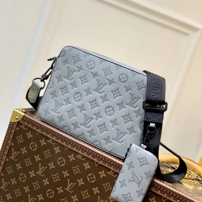 A grey monogram crossbody bag with a matching small pouch on a patterned case