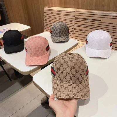 A hand holding a monogram baseball cap with more caps on the table behind it